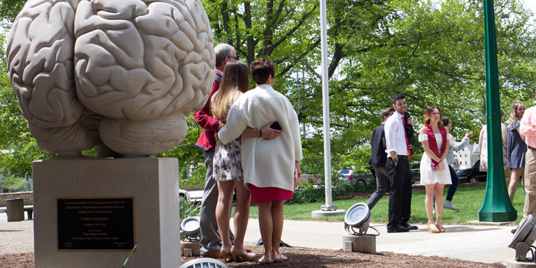 family taking pictures with graduated student in front of human brain statue