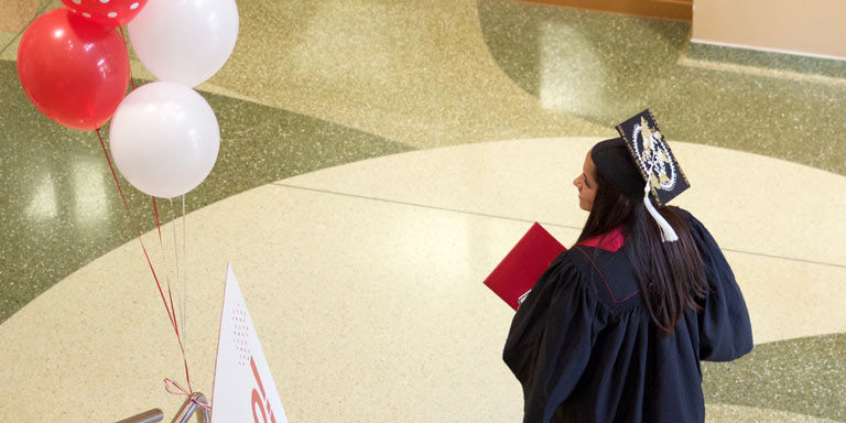 student in cap and gown walking inside a building atrium